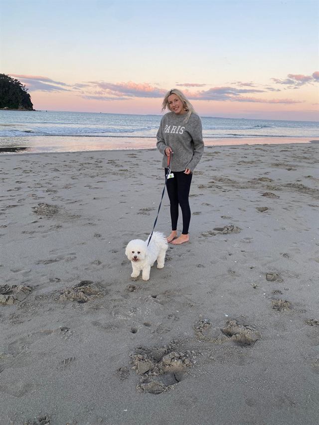 Bianca walking a small white fluffy dog on the beach at sunset