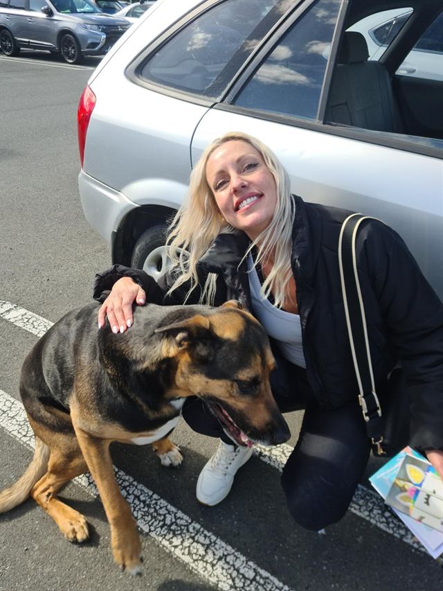 Bianca smiling and crouching beside a black and tan dog
