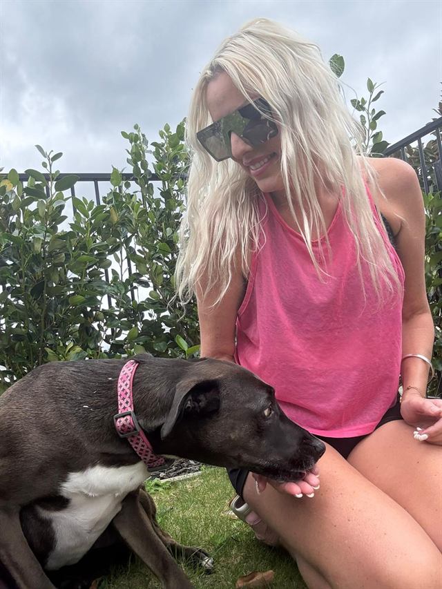 Bianca sitting on the grass with a happy brown dog in a pink collar